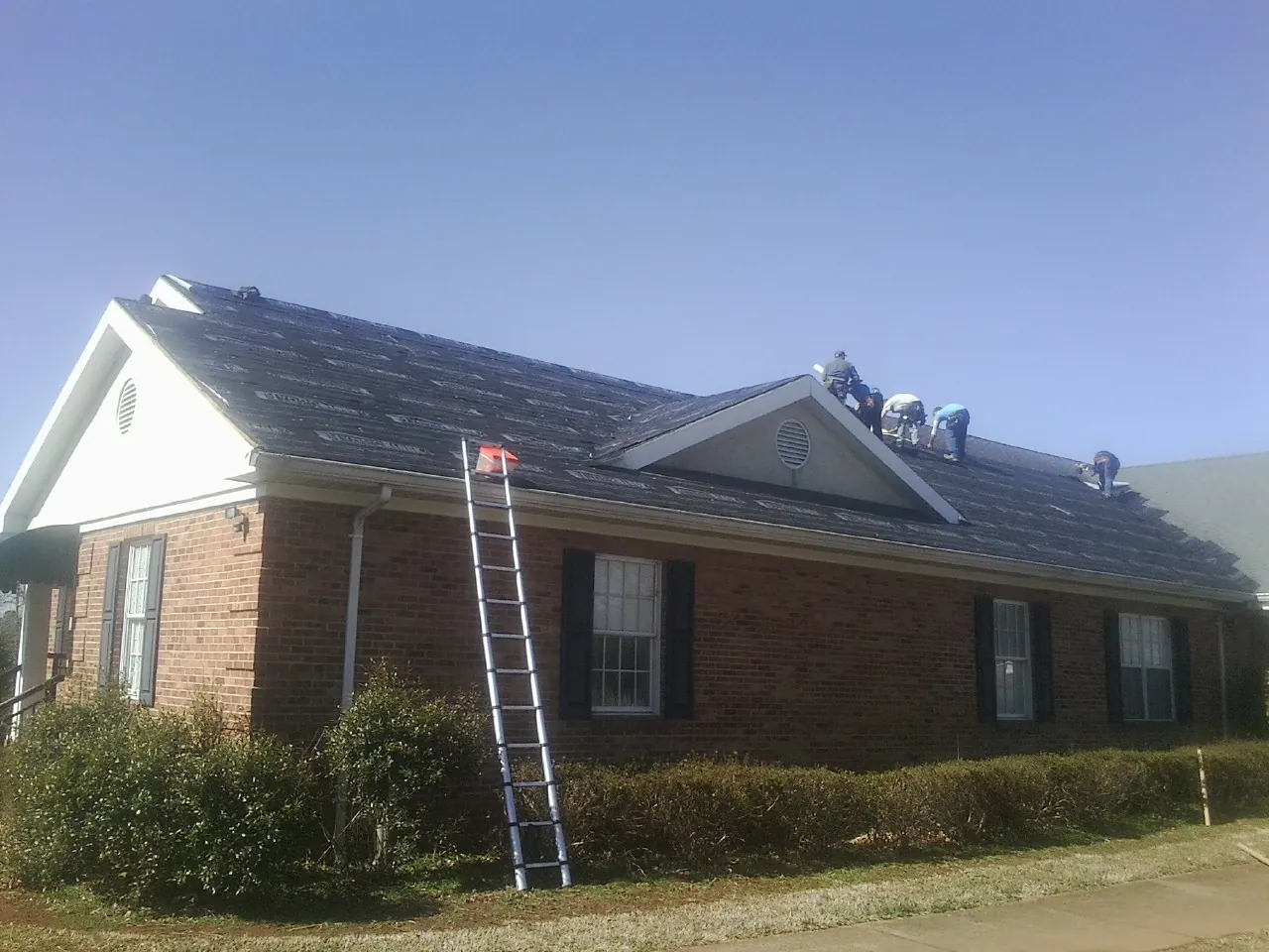 Crew tearing shingles off a brick ranch roof with a ladder set — Emergency Roof Repair work by our crew in Landisburg