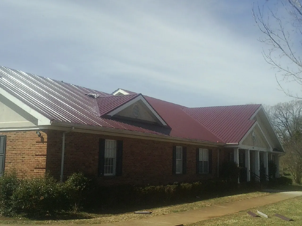 Red metal roof with gabled entries on a long brick building, from a Hail Damage Roof Repair job in Landisburg