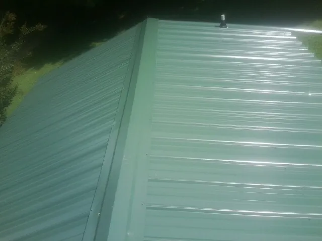 New green metal panels meeting at the ridge of a roof — Flat Roof Repair work by our crew in Landisburg