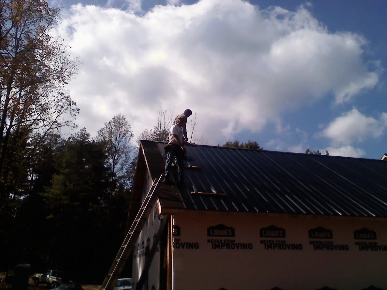 Roofer fastening dark metal panels high against a cloudy sky, from a Roof Inspection job in Landisburg