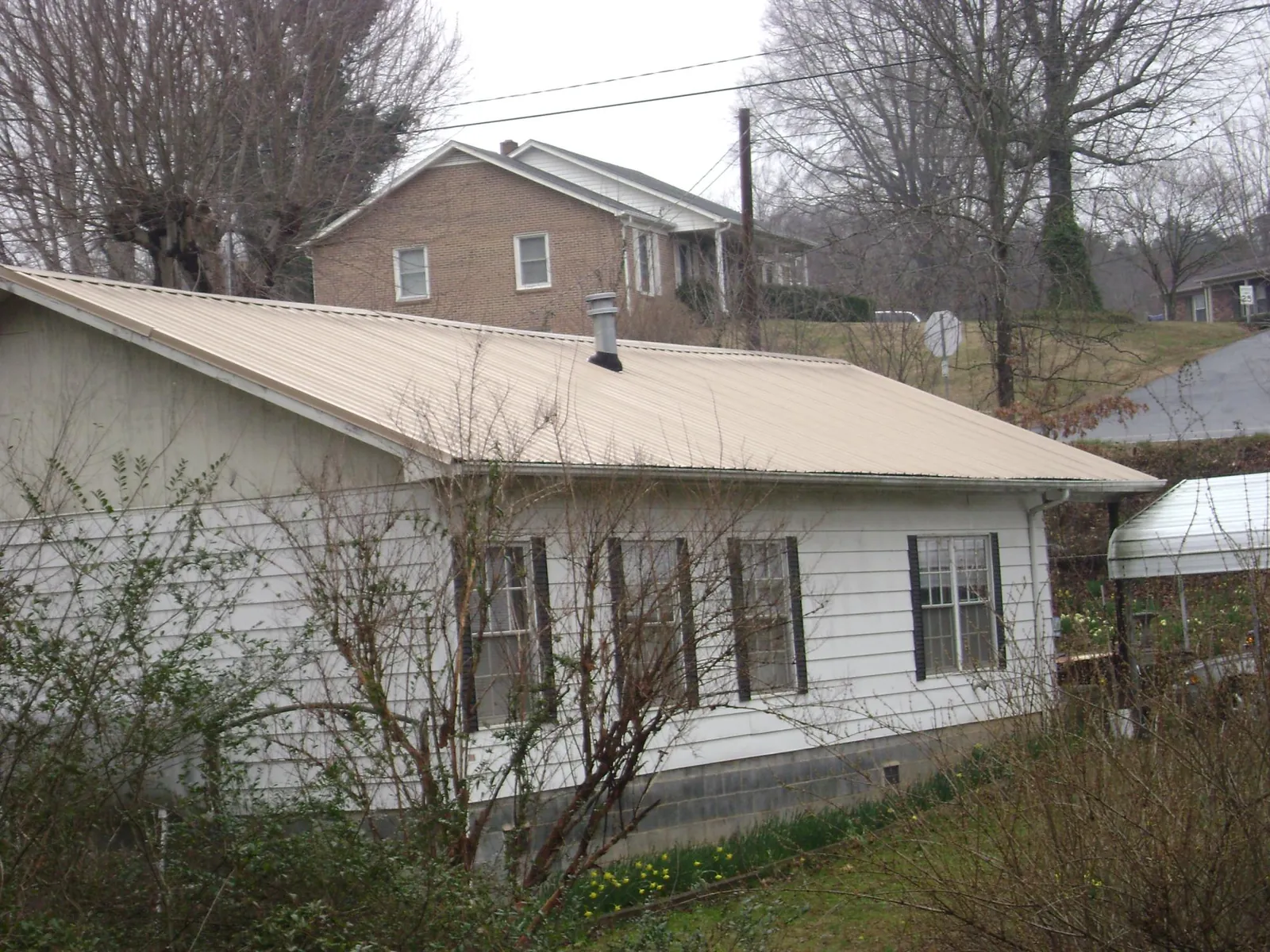 Tan metal roof on a white sided house set into a hillside — Commercial Roofing by Roofing Brothers in Landisburg